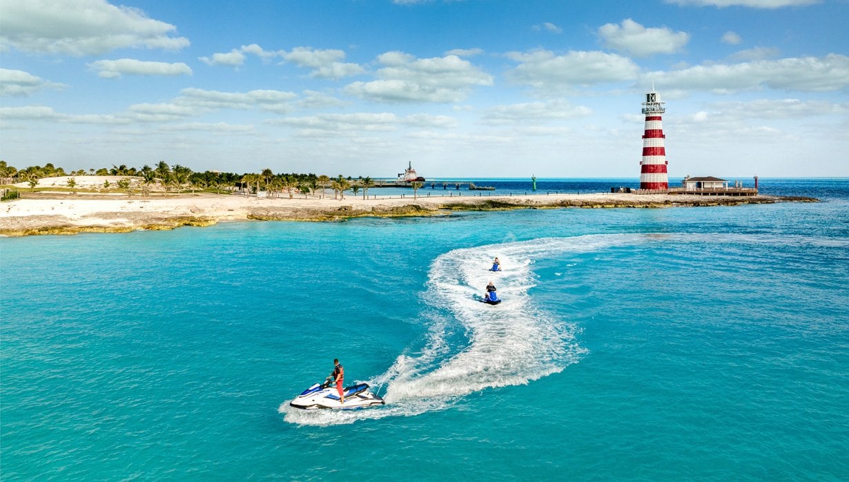 Jet skis gliding on turquoise waters near a striped lighthouse on a tropical island | MSC Cruises Jet skis gliding on turquoise waters near a striped lighthouse on a tropical island | MSC Cruises