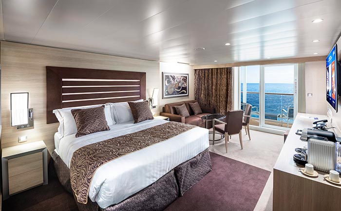 Elegant cruise suite with king-size bed, seating area, and private balcony overlooking the ocean | MSC Cruises Elegant cruise suite with king-size bed, seating area, and private balcony overlooking the ocean | MSC Cruises