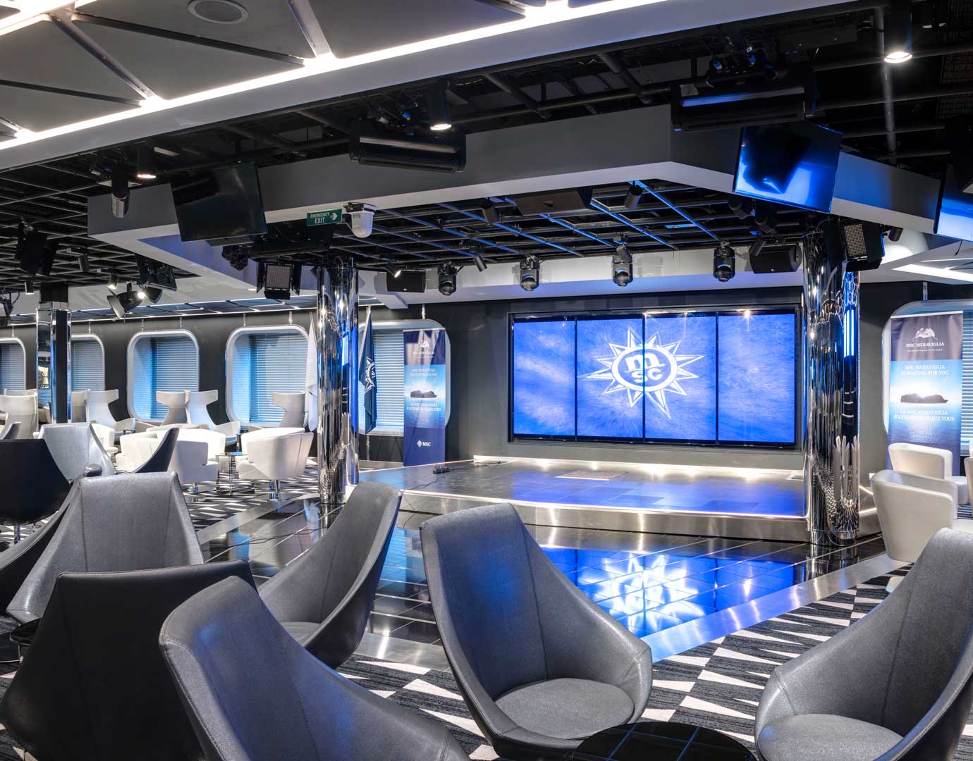 Modern lounge with sleek seating and a stage featuring the MSC logo | MSC Cruises Modern lounge with sleek seating and a stage featuring the MSC logo | MSC Cruises