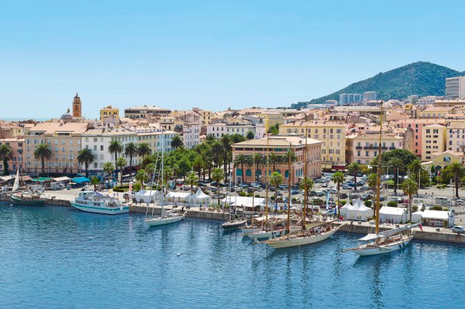 A scenic harbor with sailboats, colorful buildings, and a mountain backdrop in Ajaccio, Corsica | MSC Cruises